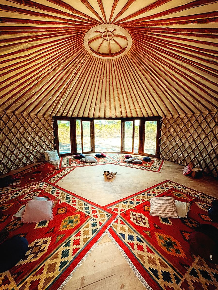 Interior of a handcrafted Yurt Workshop yurt with chestnut roof poles, rugs and a wide glass wall